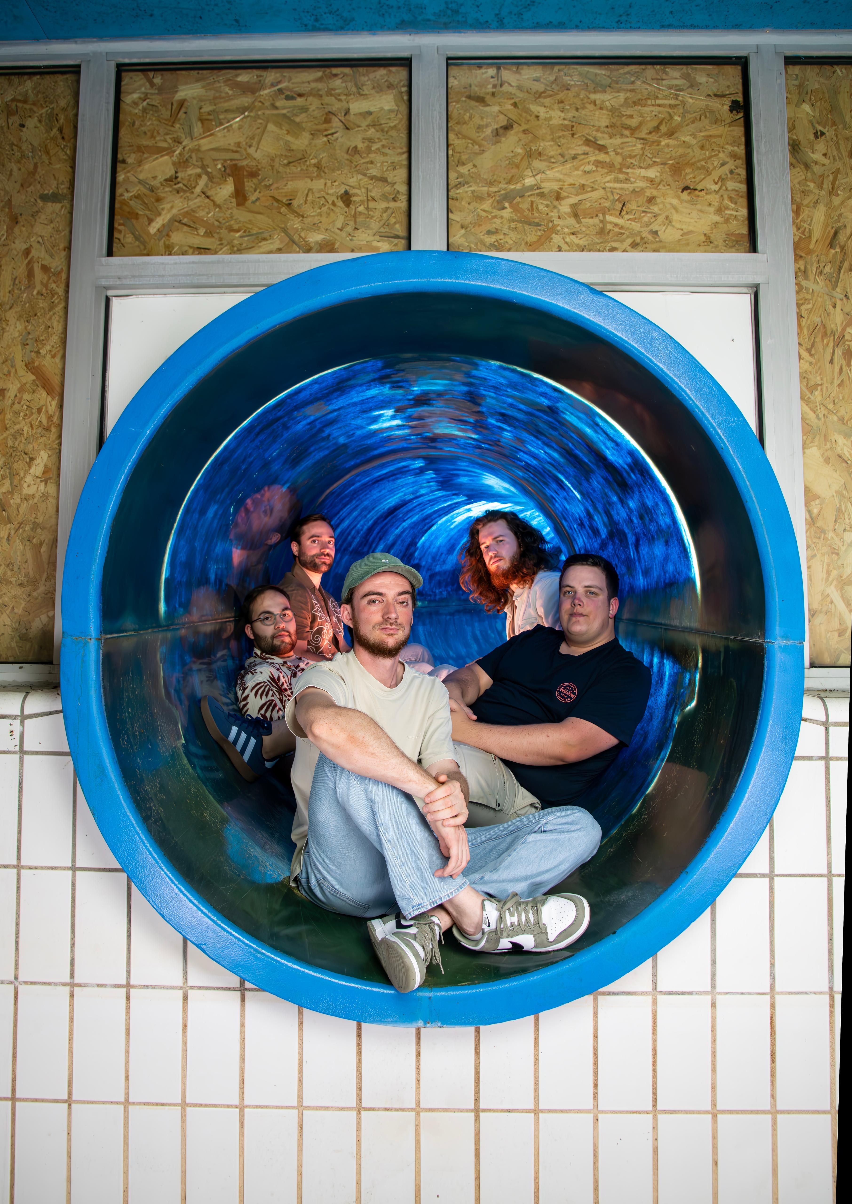 De bandleden samen in een ronde blauwe glijbaan